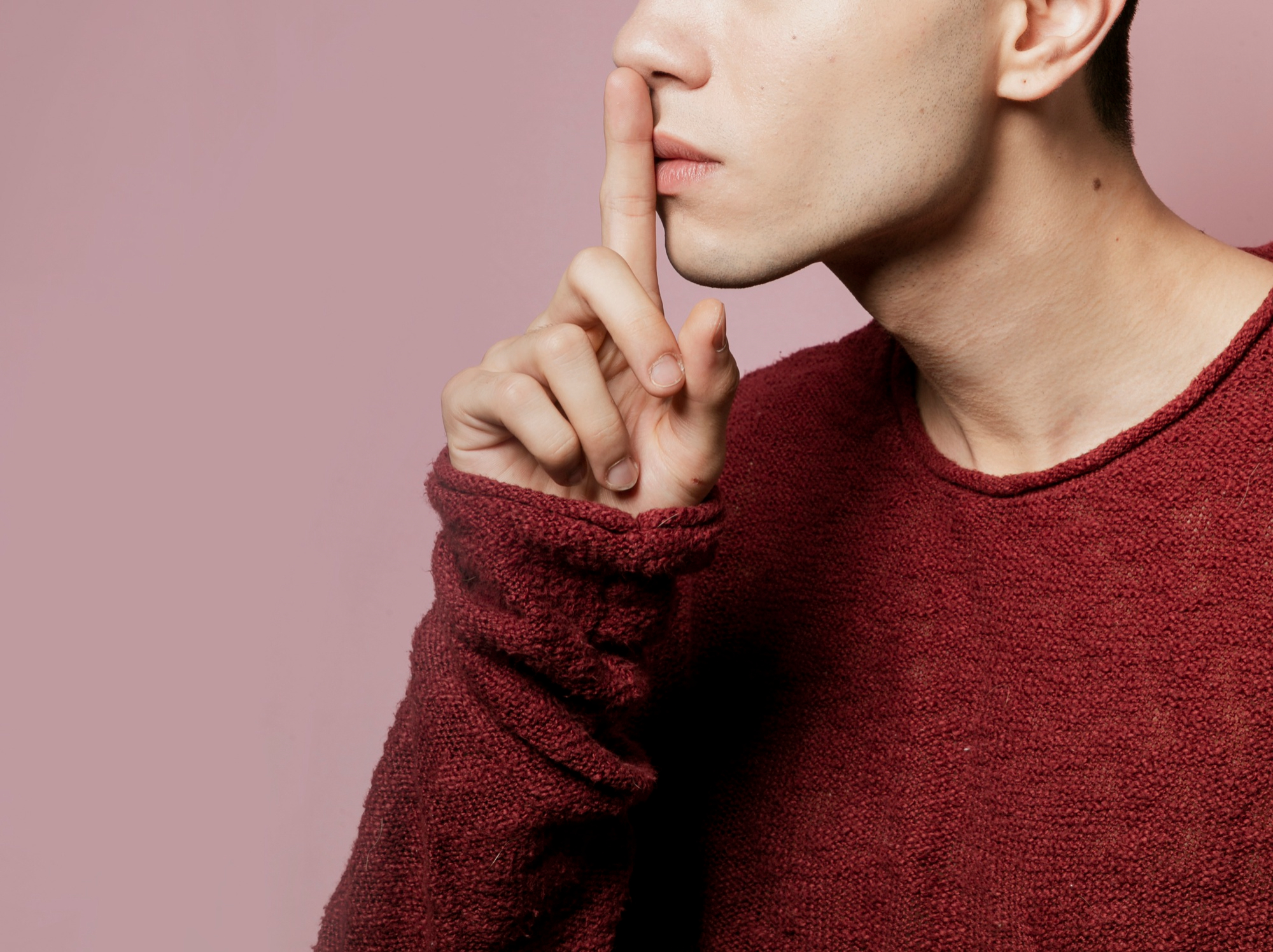 Persona con suéter rojo haciendo el gesto de silencio con el dedo índice sobre los labios