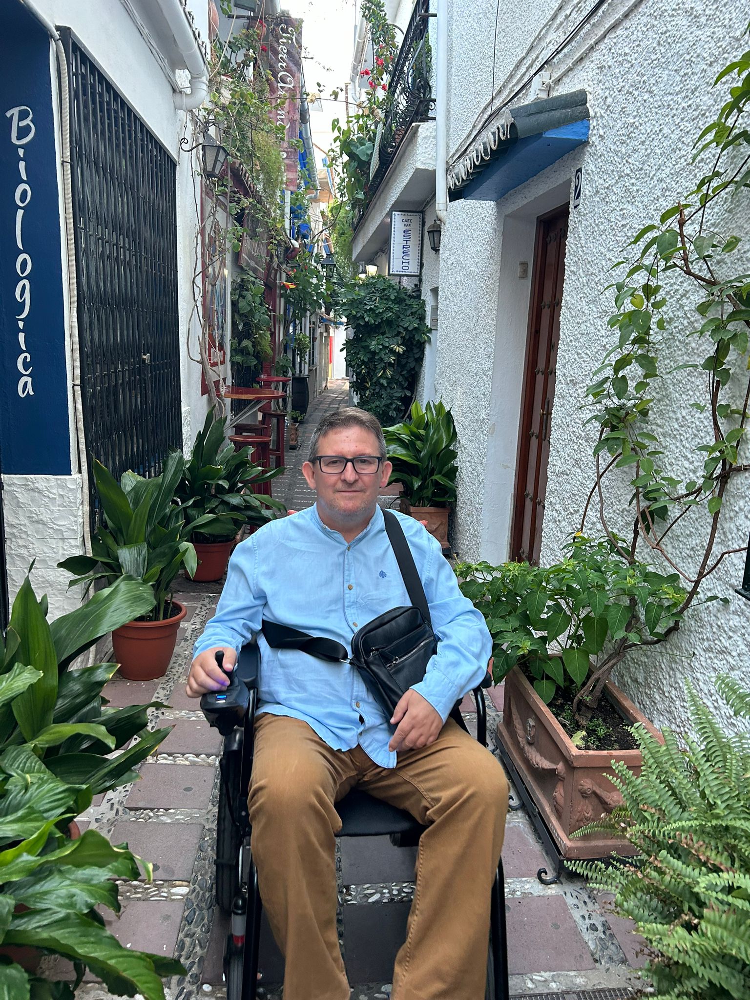 Imagen de José Luis en su silla de ruedas, en una calle estrecha llena de plantas