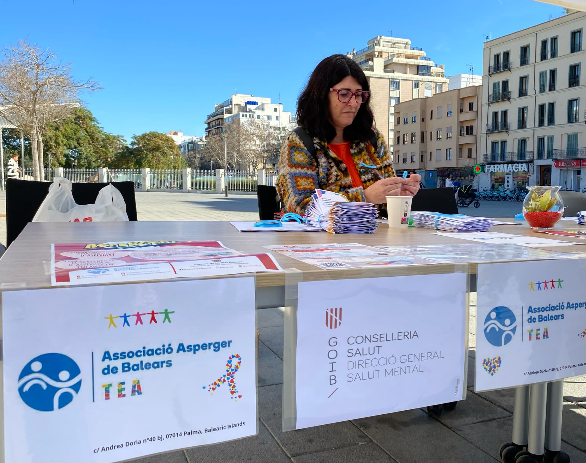 Imagen de Eva tras una mesa informativa con carteles en el frontal entre los que figura uno de la Asociación Asperger de Baleares