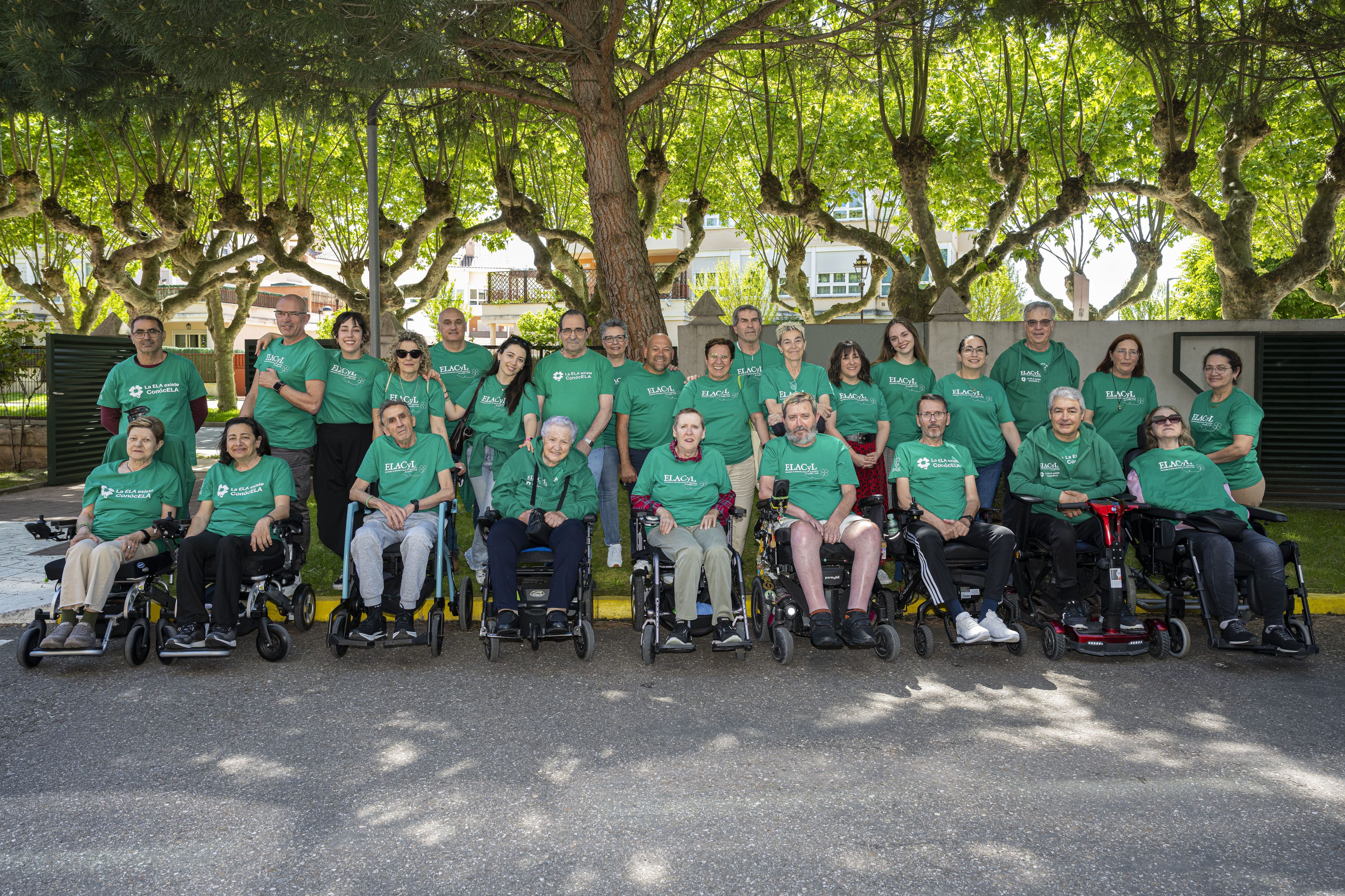 Grupo de personas en silla de ruedas con camisetas o sudaderas verdes que llevan leyendas relacionadas con la ELA 
