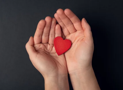 Imagen de dos manos abiertas con un corazón rojo entre ellas
