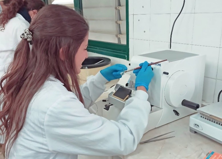 Elena con bata blanca y guantes azules manipulando material en el laboratorio   