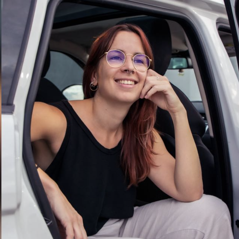 María sentada en la puerta abierta de una furgoneta blanca, con expresión relajada