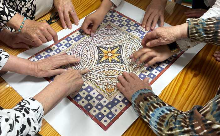 Imagen de varias manos de personas mayores alrededor de un mosaico de papel con un diseño geométrico