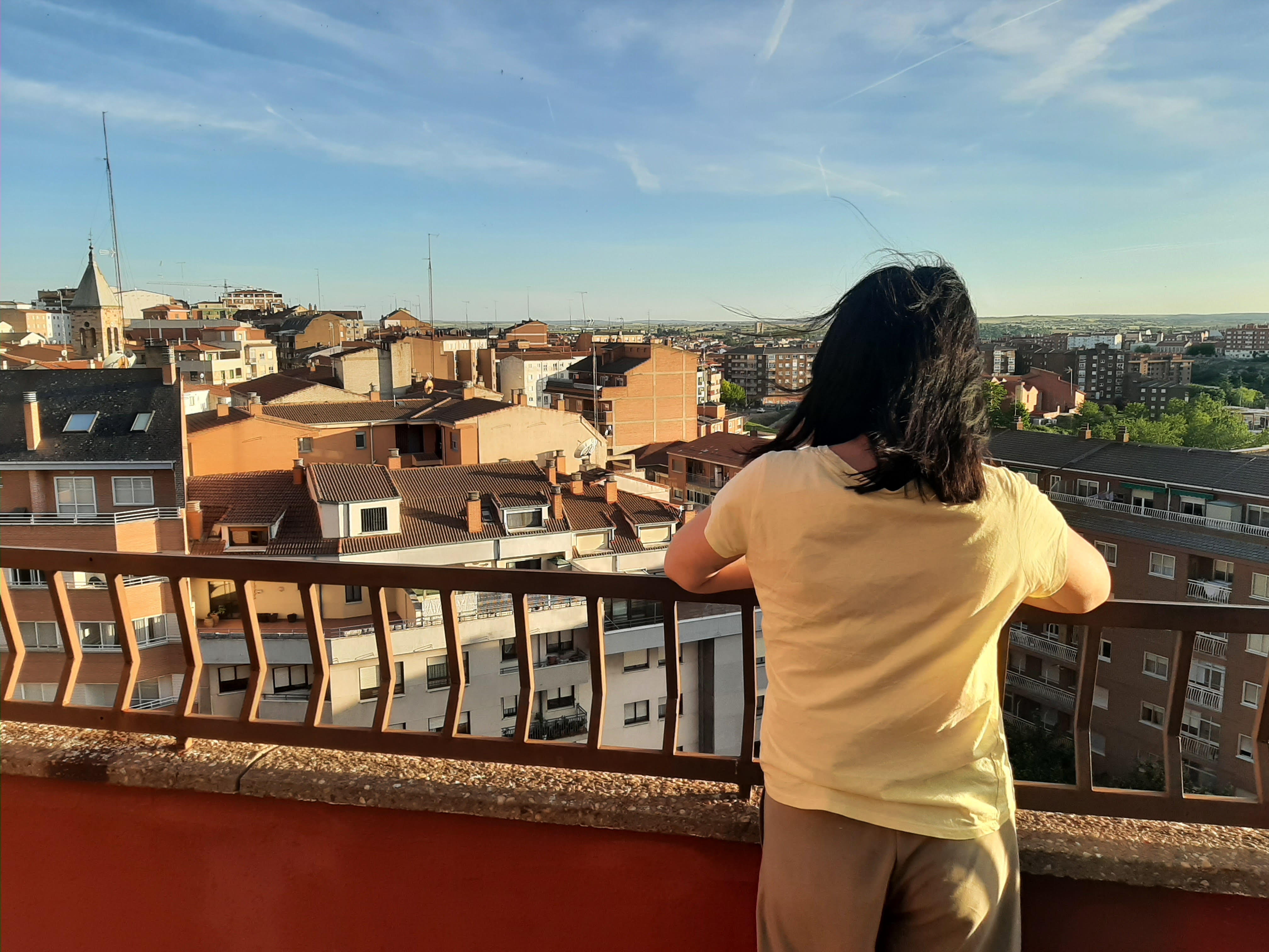 Foto de Sara de espaldas, asomada a un mirador por el que se ven las casas de un pueblo o ciudad