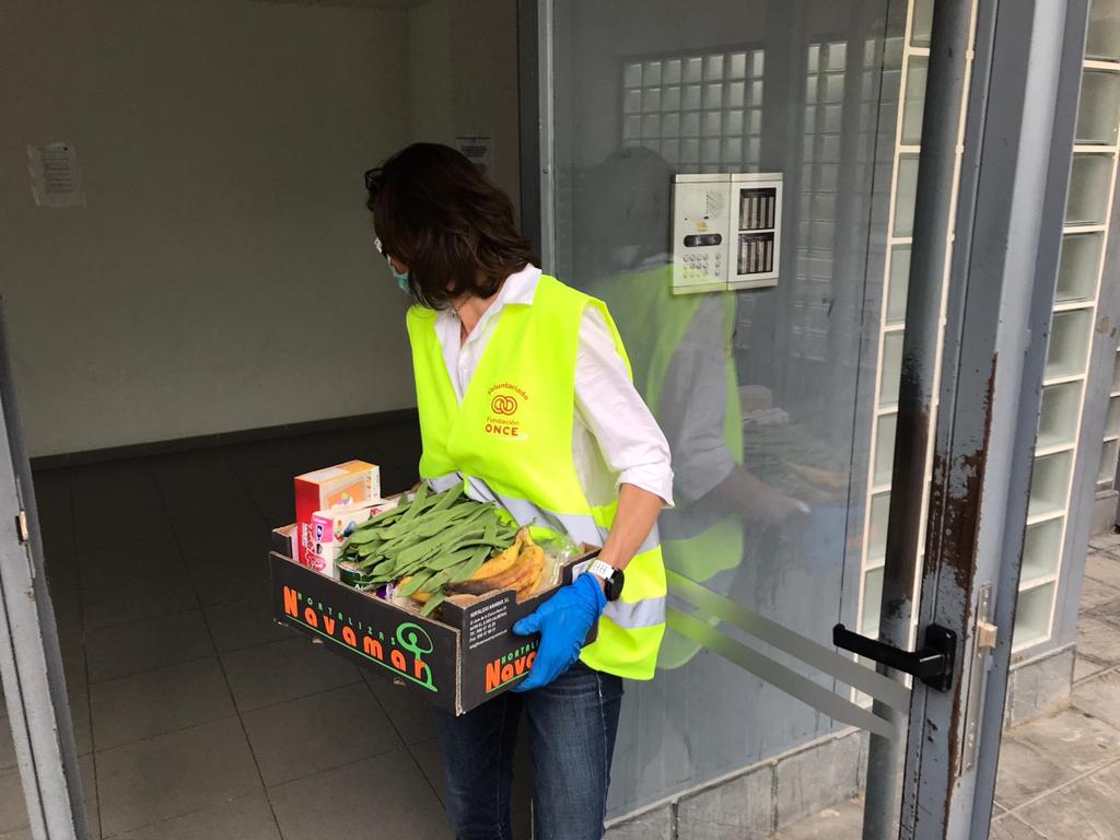 Imagen de una voluntaria de Fundación ONCE llevando una caja de comida a un domicilio 