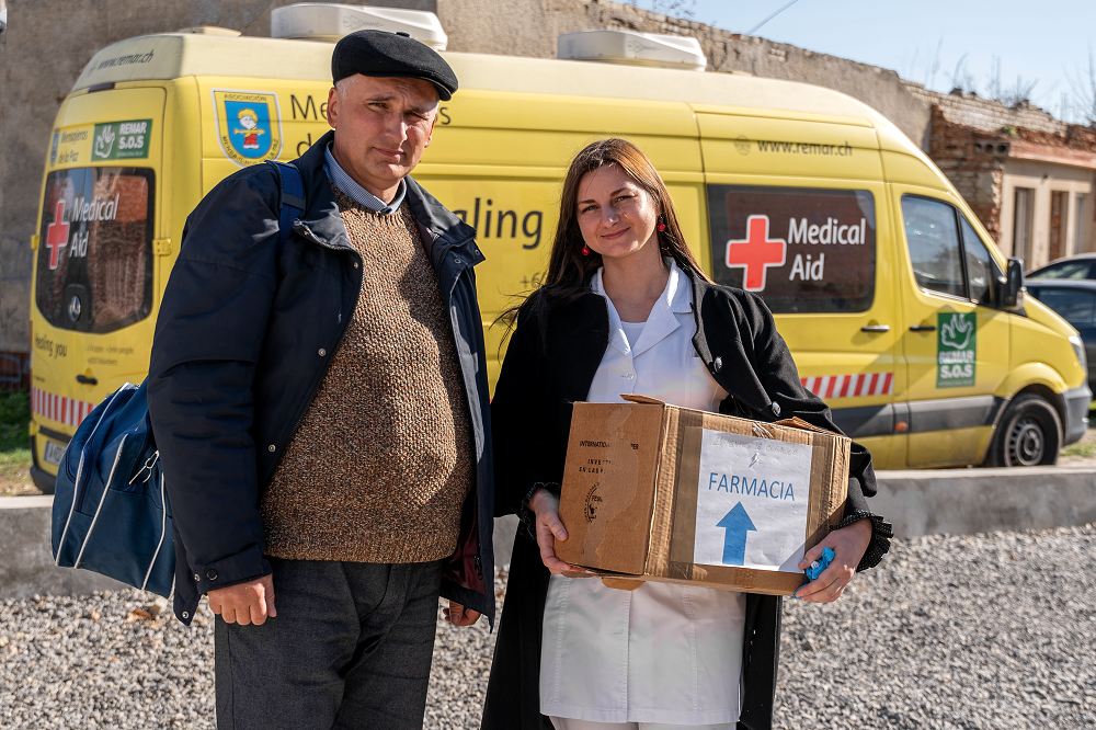 Foto en la que se ve a una cooperante llevando una caja de farmacia, acompañada de un hombre