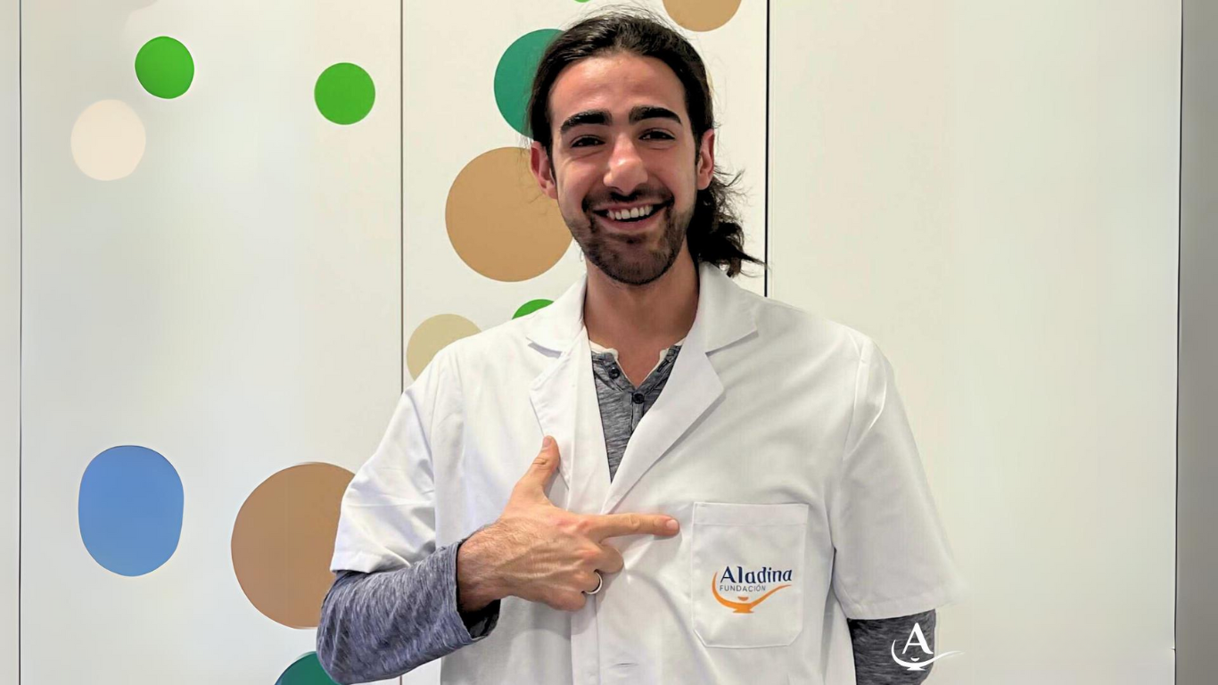 Foto de Juandi señalando el bolsillo de su bata blanca, en el que se lee "Aladina Fundación"