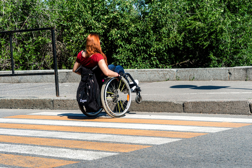 Imagen de Lucía de espaldas en su silla de ruedas curzando un paso de peatones