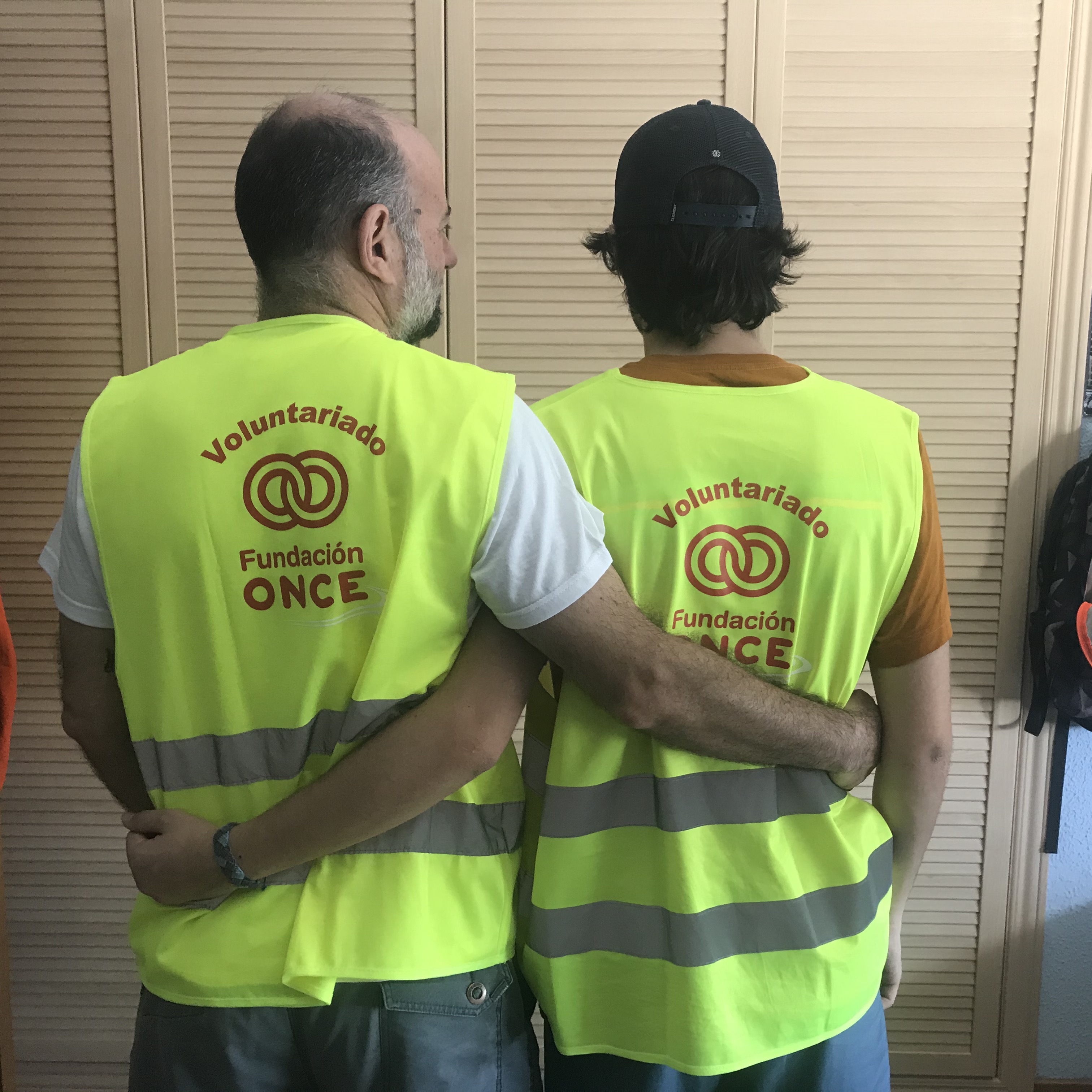 Imagen de dos personas entrelazadas por la espalda con el chaleco del voluntariado de Fundación ONCE 