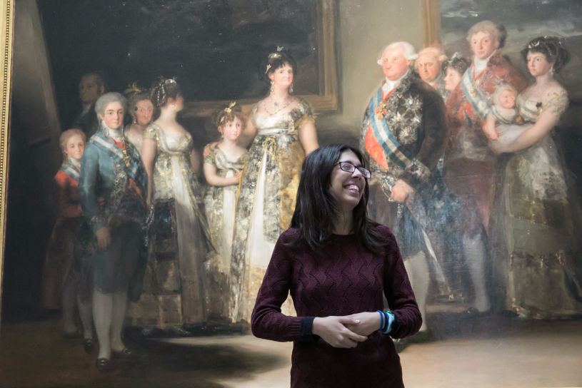 Imagen de Lucía de pie, vestida de oscuro y delante de la pintura 'La familia de Carlos IV', de Francisco de Goya 