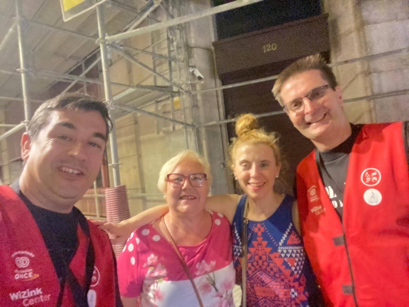 Foto de Eduardo con el chaleco de voluntario de Fundación ONCE y Wizink Center junto a dos mujeres y otro voluntario que lleva un chaleco igual al suyo