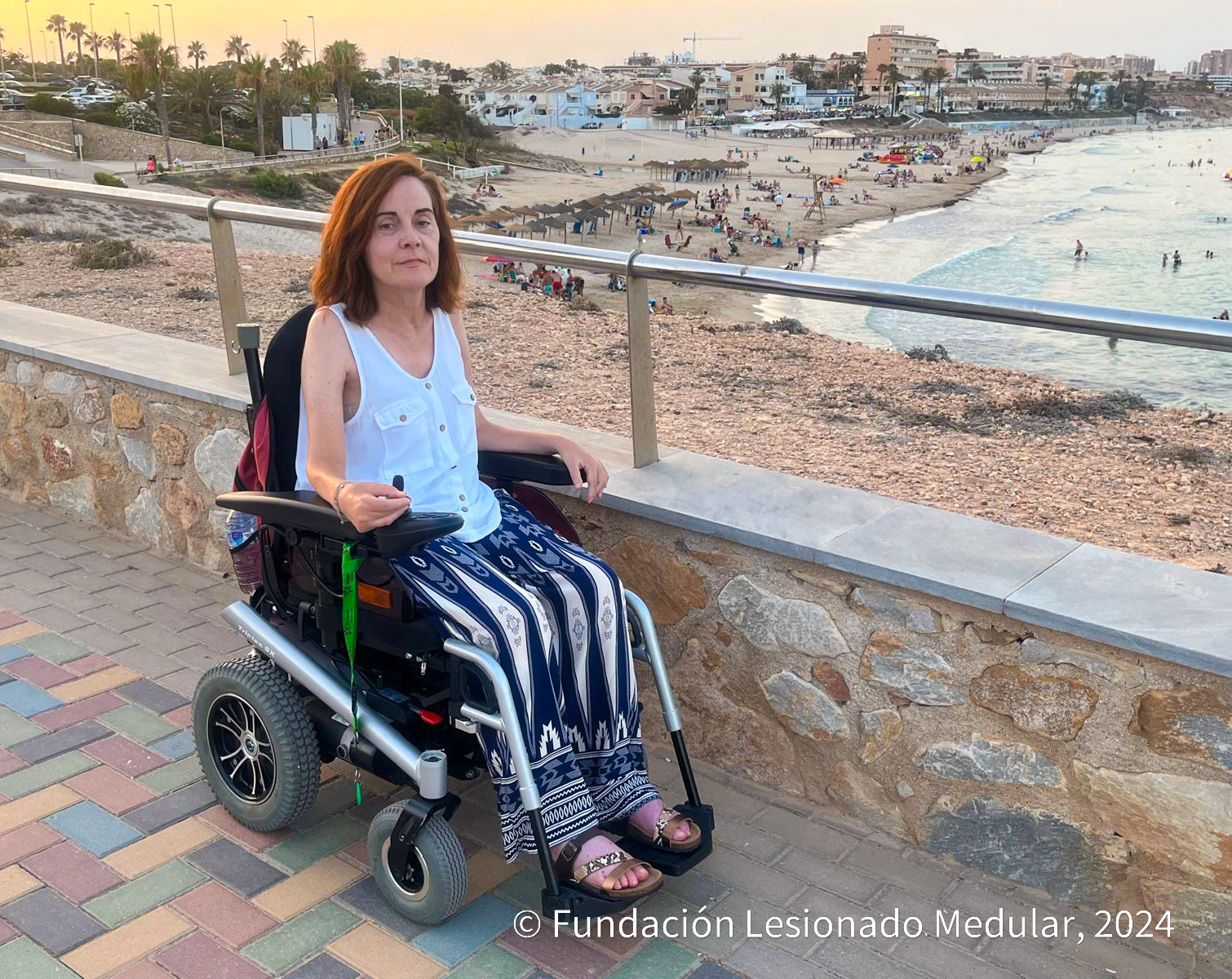 Imagen de Teresa en silla de ruedas en un paseo marítimo en el que se ve la playa