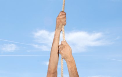 Imagen de unas manos trepando por una cuerda con el cielo azul de fondo