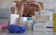 Imagen de una persona a la que no se le ve la cara, rodeada de medicamentos 