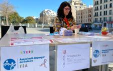 Imagen de Eva tras una mesa informativa con carteles en el frontal entre los que figura uno de la Asociación Asperger de Baleares