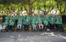 Grupo de personas en silla de ruedas con camisetas o sudaderas verdes que llevan leyendas relacionadas con la ELA 