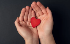 Imagen de dos manos abiertas con un corazón rojo entre ellas