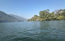 Imagen de un paisaje con agua, arboleda y montaña