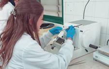 Elena con bata blanca y guantes azules manipulando material en el laboratorio   