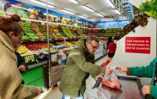 Imagen de una sección de frutas y verduras del supermercado en la que se ve a varias personas, una de ellas pesando el producto. A la derecha de la imagen hay un cartel que reza: ‘Por higiene es obligatorio el uso de guantes’