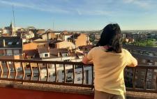 Foto de Sara de espaldas, asomada a un mirador por el que se ven las casas de un pueblo o ciudad