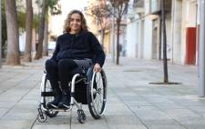 Fabiola en silla de ruedas sonriente sobre una acera, vestida con ropa oscura.