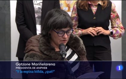 Foto de Gotzone hablando frente a un micrófono en la que se ve también un cartel que dice: “Gotzone Mariñelarena, presidenta de ANPHEB. ¿Y la espina bífida, qué?”.