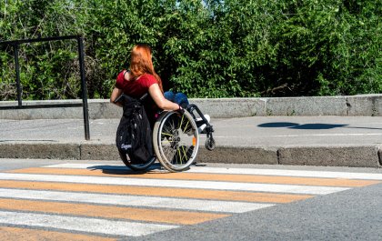 Imagen de Lucía de espaldas en su silla de ruedas curzando un paso de peatones