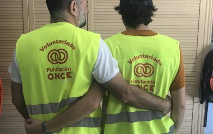 Imagen de dos personas entrelazadas por la espalda con el chaleco del voluntariado de Fundación ONCE 