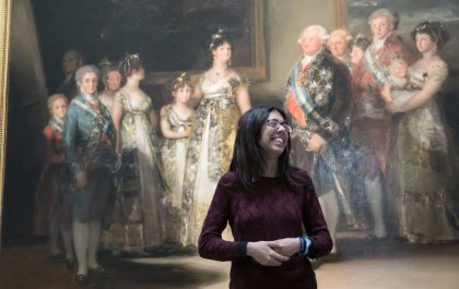 Imagen de Lucía de pie, vestida de oscuro y delante de la pintura 'La familia de Carlos IV', de Francisco de Goya 