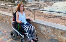 Imagen de Teresa en silla de ruedas en un paseo marítimo en el que se ve la playa