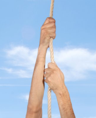 Imagen de unas manos trepando por una cuerda con el cielo azul de fondo
