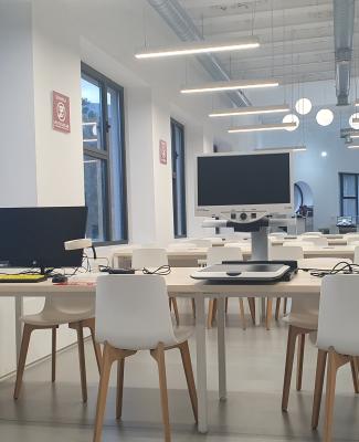 Sala de biblioteca donde se ven puestos para el trabajo de usuarios y una estantería llena de libros  