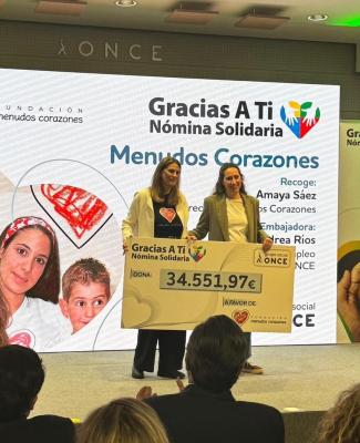 Foto de Andrea entregando un cheque gigante a la representante de Menudos Corazones en el que se le la cifra donada: 34.551,97 