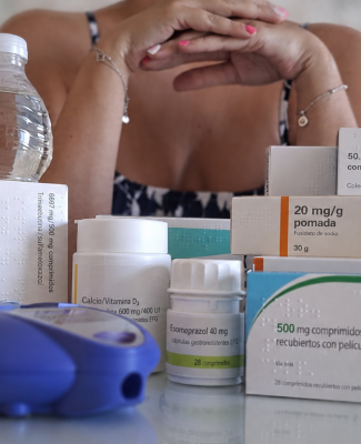 Imagen de una persona a la que no se le ve la cara, rodeada de medicamentos 