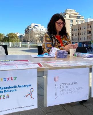 Imagen de Eva tras una mesa informativa con carteles en el frontal entre los que figura uno de la Asociación Asperger de Baleares