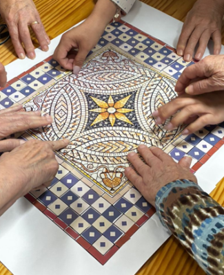 Imagen de varias manos de personas mayores alrededor de un mosaico de papel con un diseño geométrico
