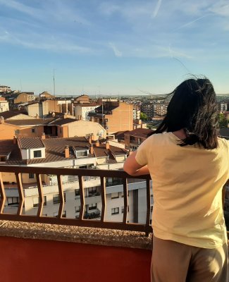 Foto de Sara de espaldas, asomada a un mirador por el que se ven las casas de un pueblo o ciudad