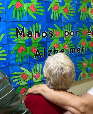 Imagen de personas mayores de espaldas. mirando un mural en el que se ven manos verdes y corazones rojos y se lee: “Manos por el alzheimer”