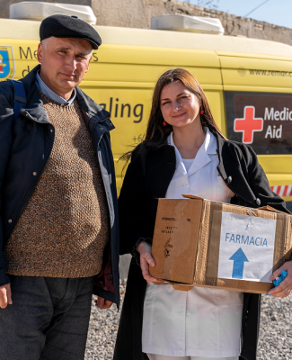 Foto en la que se ve a una cooperante llevando una caja de farmacia, acompañada de un hombre  