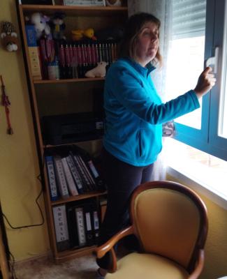 Imagen de Raquel, de pie delante de una estantería con libros y ante una ventana que va a abrir