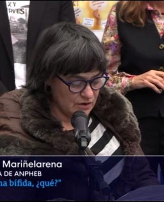Foto de Gotzone hablando frente a un micrófono en la que se ve también un cartel que dice: “Gotzone Mariñelarena, presidenta de ANPHEB. ¿Y la espina bífida, qué?”.