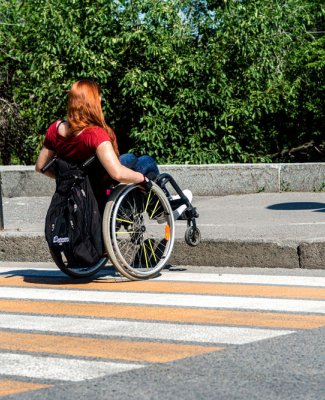 Imagen de Lucía de espaldas en su silla de ruedas curzando un paso de peatones