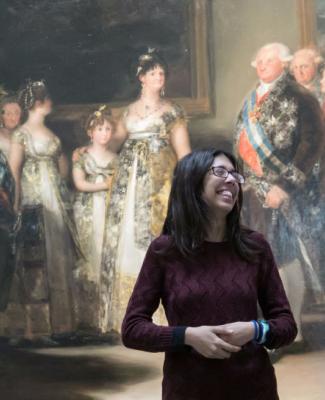 Imagen de Lucía de pie, vestida de oscuro y delante de la pintura 'La familia de Carlos IV', de Francisco de Goya 