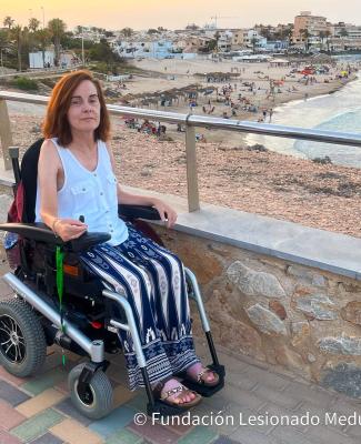 Imagen de Teresa en silla de ruedas en un paseo marítimo en el que se ve la playa